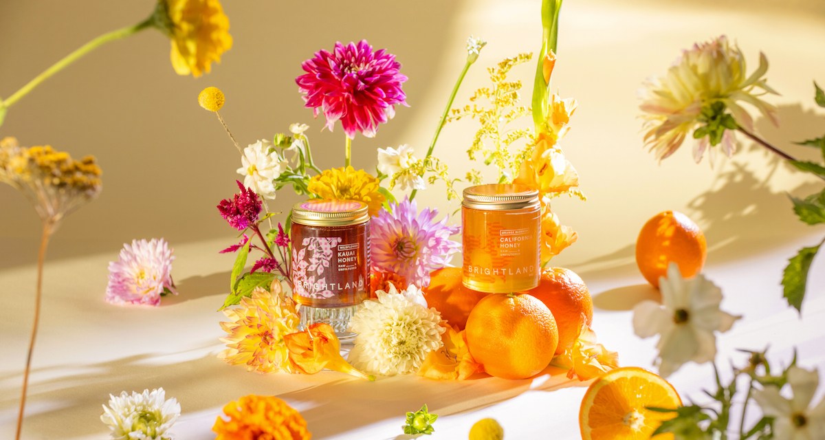 Honey bottles displayed on a table alongside fresh flowers and oranges