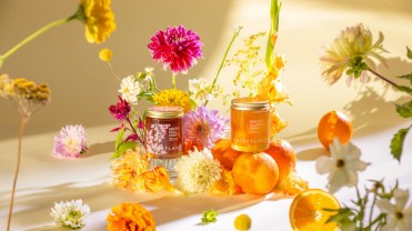 Honey bottles displayed on a table alongside fresh flowers and oranges