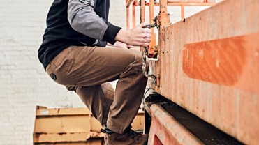 Photograph of a man wearing work cloths and climbing to the top of a forklift.