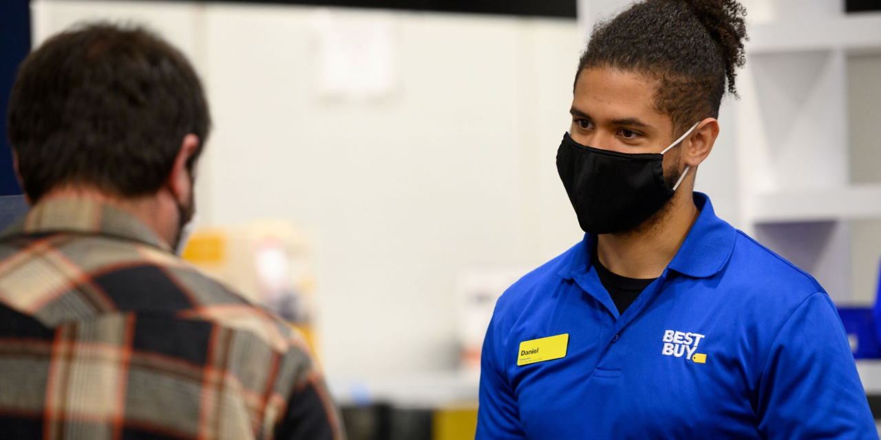 Man in blue Best Buy polo wearing a mask talking with another man