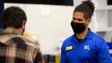 Man in blue Best Buy polo wearing a mask talking with another man