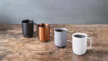 Ember coffee mugs in black, copper, gray and white lined up on a wooden table