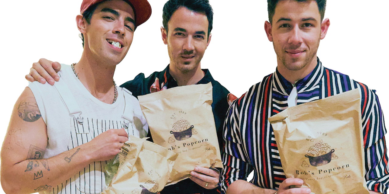 Photograph of the Jonas Brothers holding bags of Rob's Backstage Popcorn.