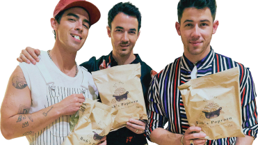 Photograph of the Jonas Brothers holding bags of Rob's Backstage Popcorn.