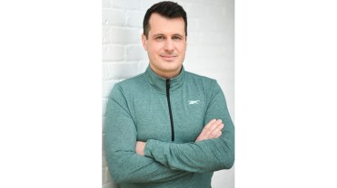 Man in green zip up stands with arms crossed against a wall