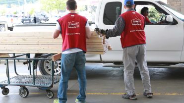 Workers in red Lowe's branded vests pile plywood into white truck