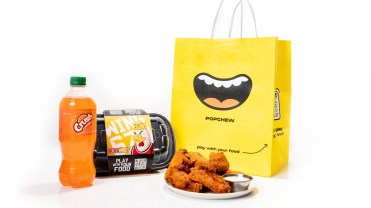 Chicken wings on a plate next to a yellow Popchew bag and orange crush soda
