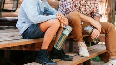 Two kids sitting on a bench holding water bottles
