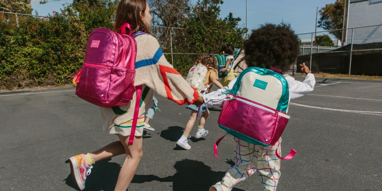 Two children holding hands wearing hot pink metallic backpacks