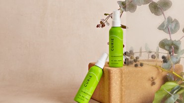 Two bottles of Curie eucalyptus full body deodorant spray in green bottles on top of a cardboard box