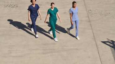 Three people in scrubs from Kindthread walk across a parking lot