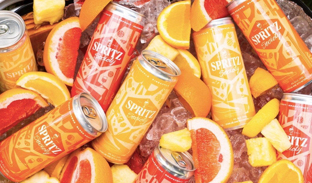 Bucket of yellow, red and orange Spritz Society cans in ice with orange and pineapple slices
