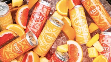 Bucket of yellow, red and orange Spritz Society cans in ice with orange and pineapple slices
