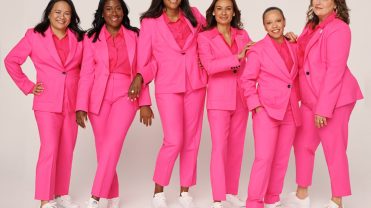 A group of women wearing hot pink suits and white sneakers in a photo shoot.