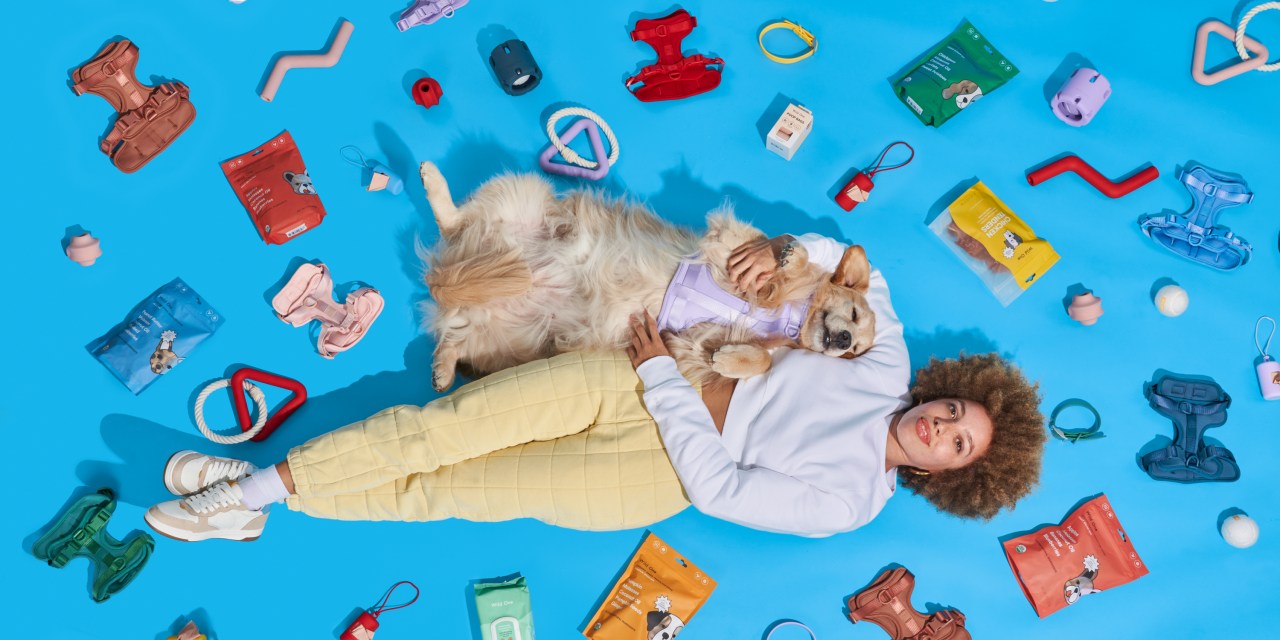 A woman and a golden retriever lies on the floor with several Wild One products.