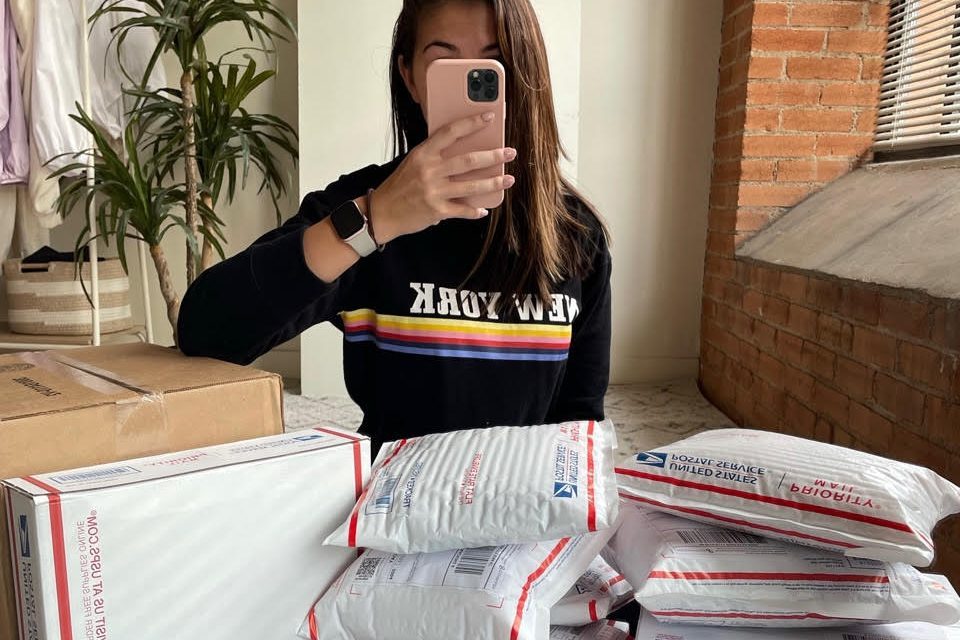 A woman takes a selfie with many postal packages around her.