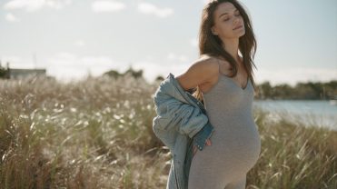 Pregnant women in a grey jumpsuit in a field