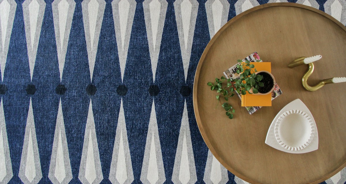 Coffee table, with plant, candle holder and books set atop a blue and white-striped rug.