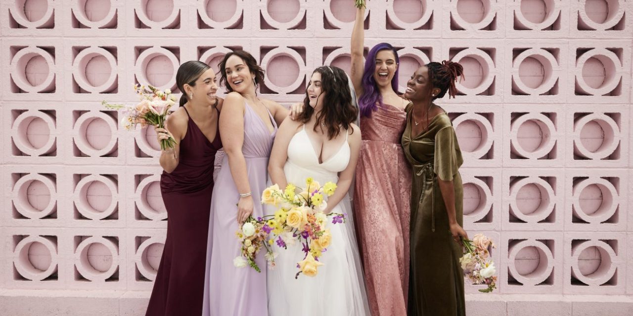 Four bridesmaids surround a bride in a white dress smiling and laughing.