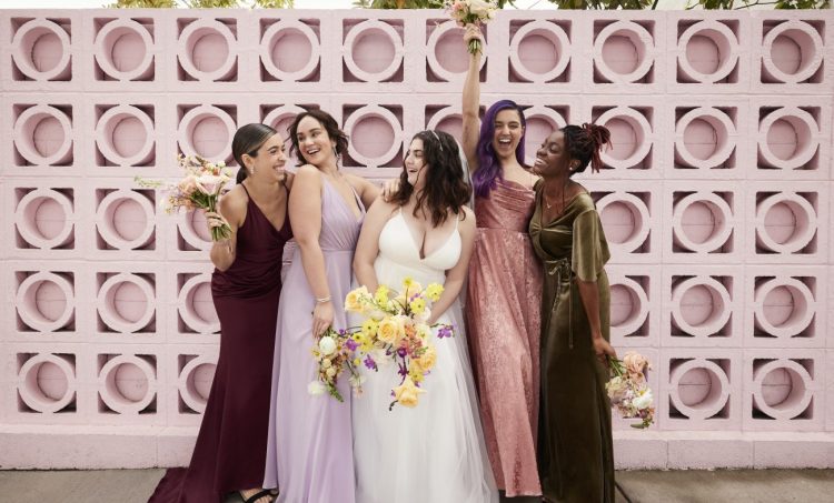 Four bridesmaids surround a bride in a white dress smiling and laughing.