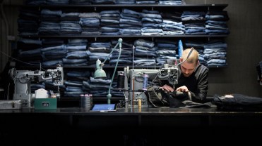 A man bends over a sewing table with a pair of denim jeans.