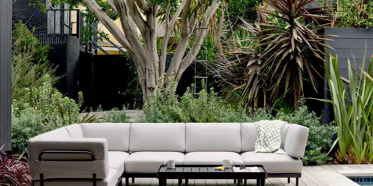 A light grey couch on a black frame in a tree-lined backyard.