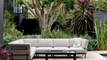 A light grey couch on a black frame in a tree-lined backyard.