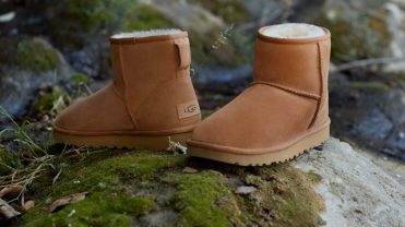 A pair of short fuzzy chestnut-colored boots posed outside on a rock.