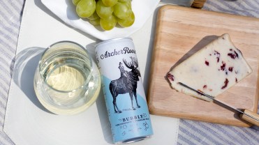 Archer Roose's canned wine in between a slice of cheese and a glass of wine.