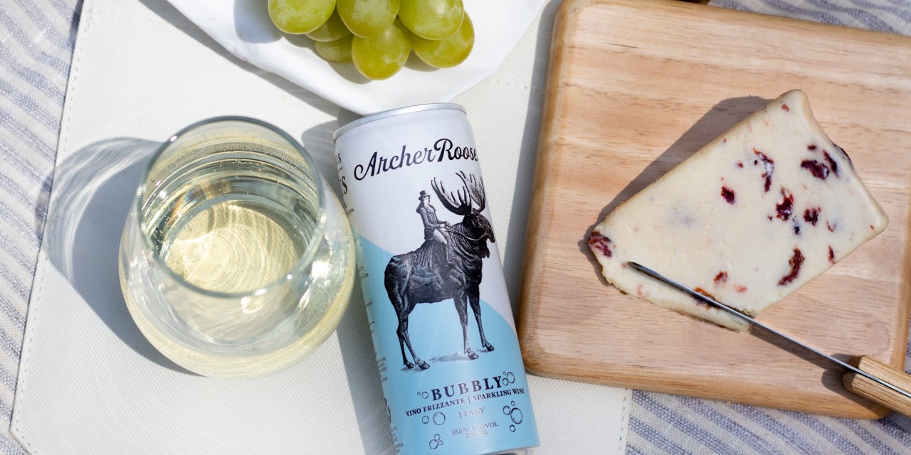 Archer Roose's canned wine in between a slice of cheese and a glass of wine.