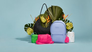Assortment of hot pink, lime green and bright blue handbags and backpacks on a blue background, surrounded by leaves