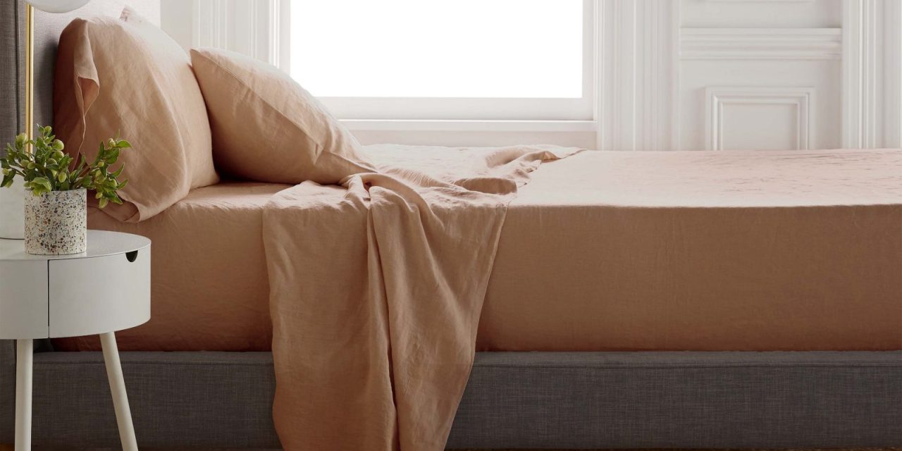 A bed with terra cotta sheets in front of a sunny window