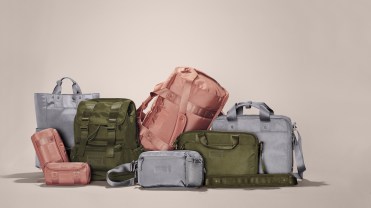 A variety of pink, grey and olive backpacks and duffel bags on a tan background