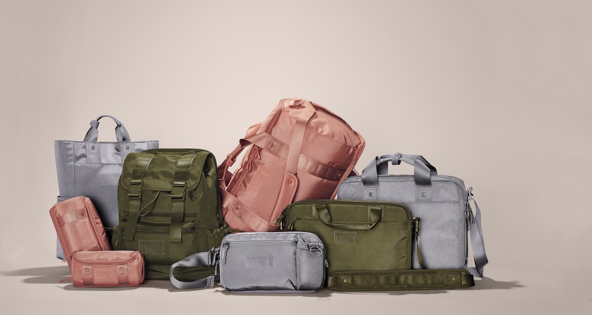 A variety of pink, grey and olive backpacks and duffel bags on a tan background