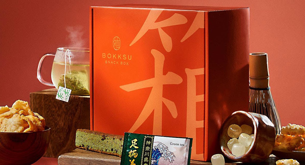 A red Japanese subscription box with products like tea and candy sits on a red background