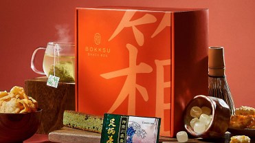 A red Japanese subscription box with products like tea and candy sits on a red background