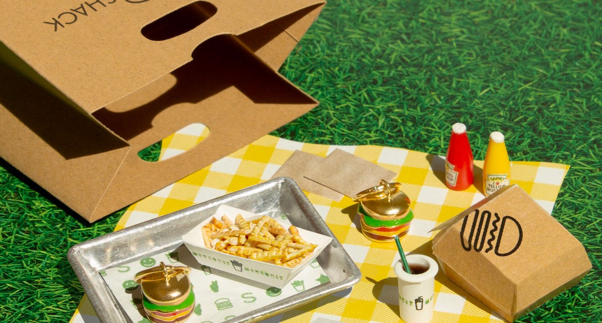 French fries and miniature burger earrings on a yellow and white checkered picnic blanket, next to a Shake Shack bag.
