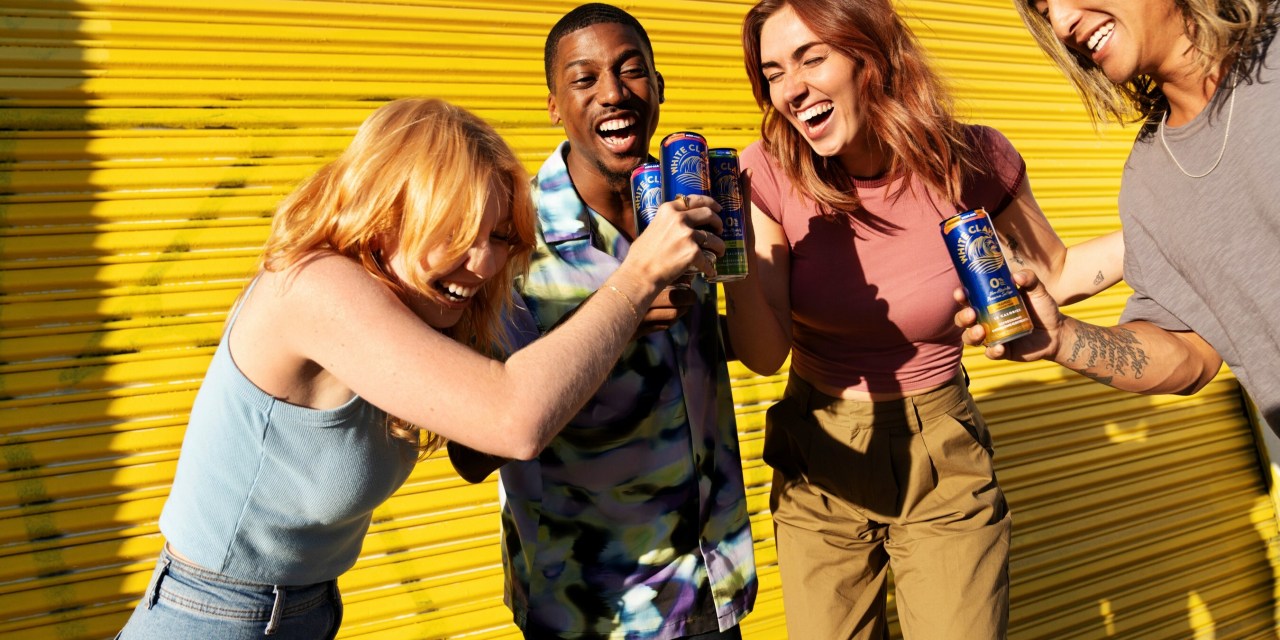 A group of people laughing and drinking White Claw's 0% alcohol seltzer.