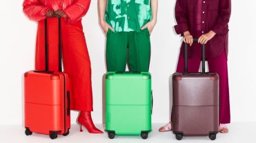 Three models displaying carry-on luggage in red, green and black shades