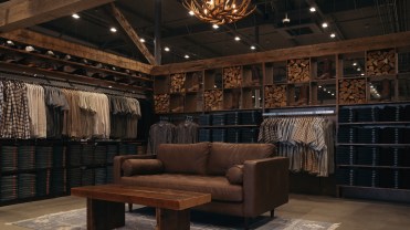 Brown leather couch and wooden side table in a retail space, surrounded by rows of button-down shirts