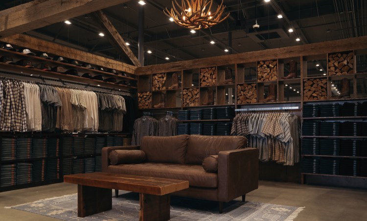 Brown leather couch and wooden side table in a retail space, surrounded by rows of button-down shirts