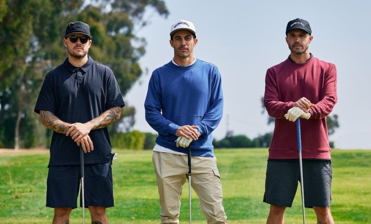 Three golfers stand on a course in Municipal clothing