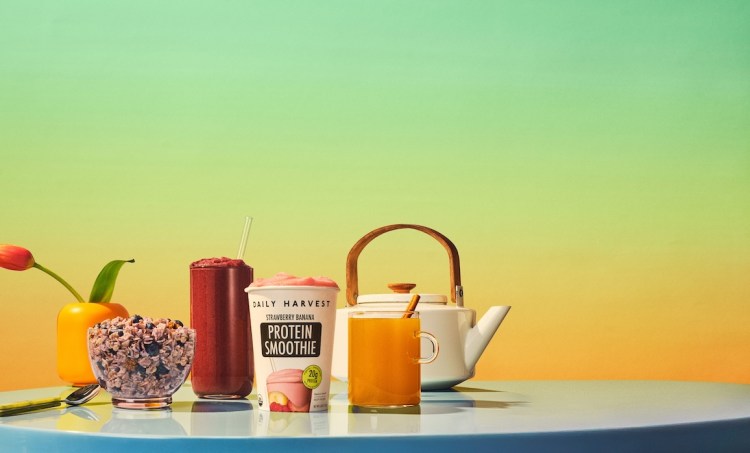 Daily Harvest smoothie, elixir and oat bowl on a blue table against a green and yellow background.