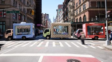 Glass moving trucks bedazzled with the "Urban Outfitters" company name sit on a New York City street