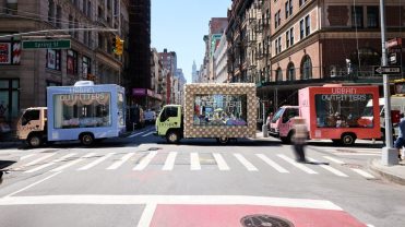 Glass moving trucks bedazzled with the "Urban Outfitters" company name sit on a New York City street