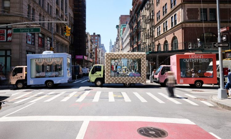 Glass moving trucks bedazzled with the "Urban Outfitters" company name sit on a New York City street