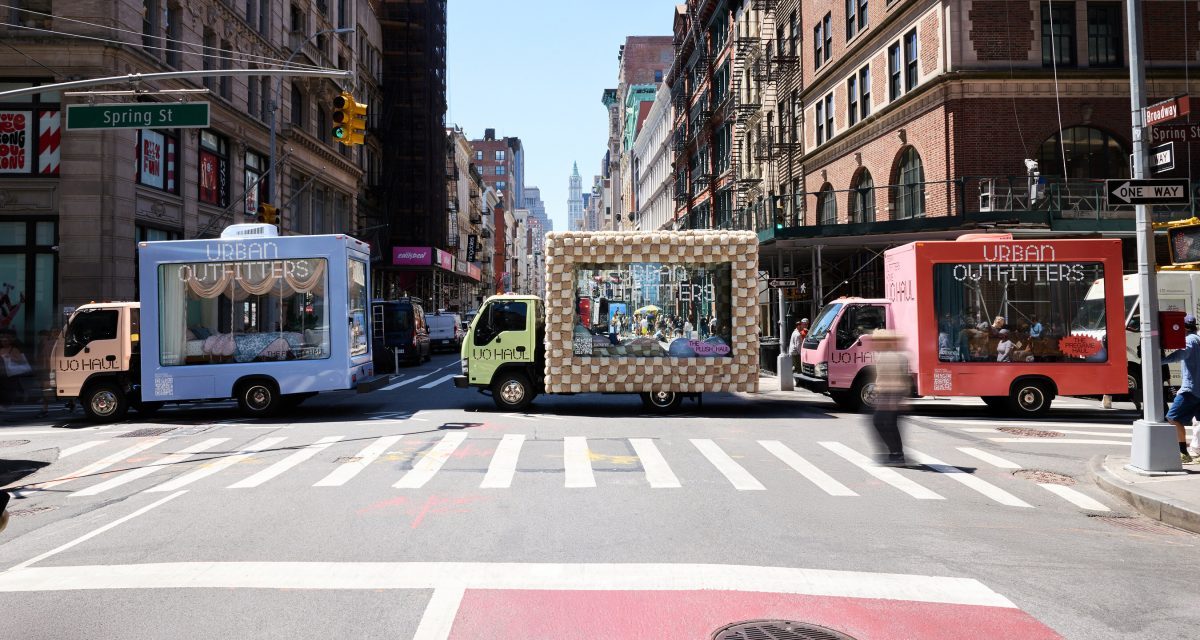 Glass moving trucks bedazzled with the "Urban Outfitters" company name sit on a New York City street