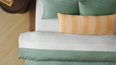 Green sateen sheets on a bed with a yellow striped pillow