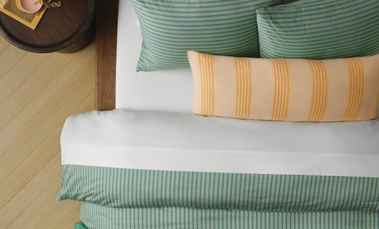 Green sateen sheets on a bed with a yellow striped pillow