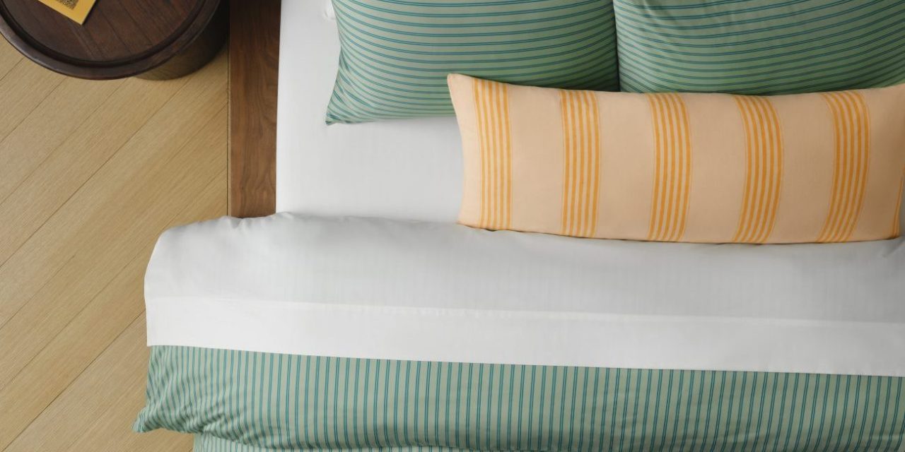 Green sateen sheets on a bed with a yellow striped pillow